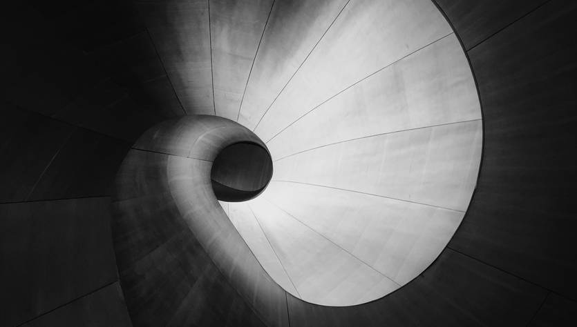 La imagen muestra una espiral arquitectónica en tonos gris y negro que transmite una sensación de fluidez y modernidad.