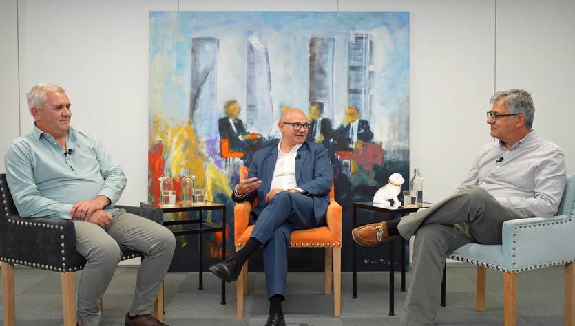 Tres hombres conversan en un ambiente profesional frente a una pintura colorida.