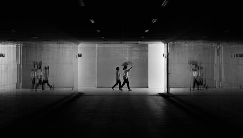 Dos personas caminan por un pasillo iluminado en un entorno oscuro.