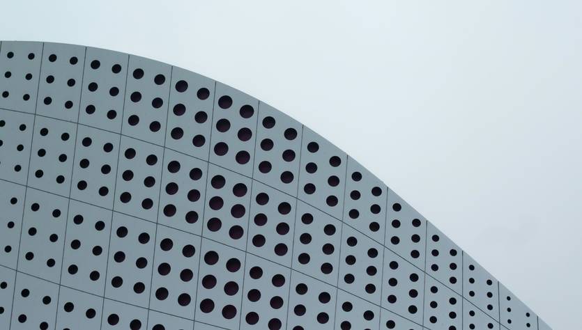 Una moderna fachada de edificio con un diseño curvo y perforaciones circulares.