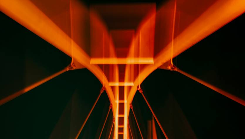 La imagen muestra un puente iluminado con luces de tono naranja contra un fondo oscuro.