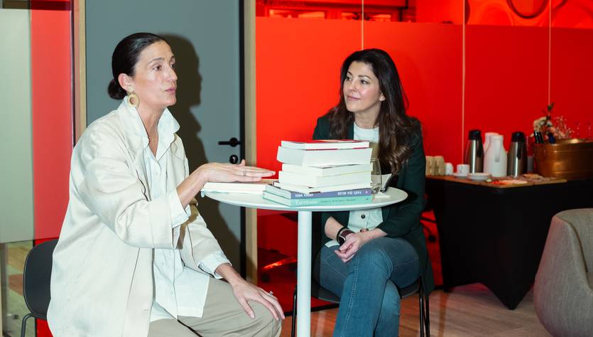 Dos mujeres conversan sentadas en un ambiente moderno con decoración roja.