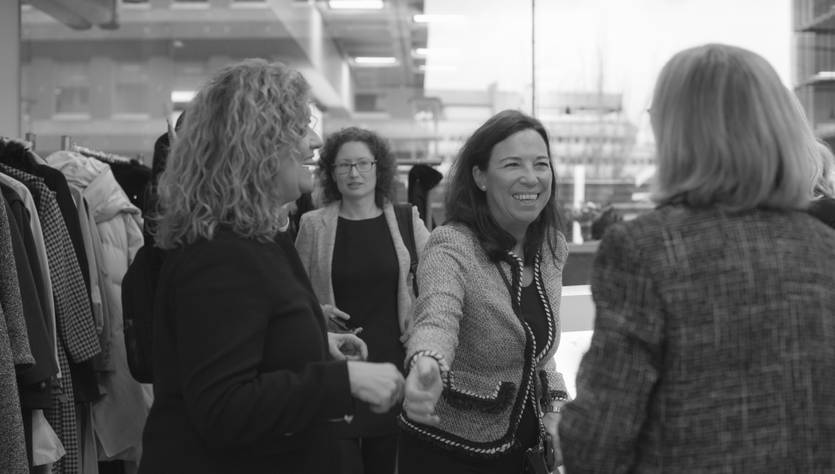 Un grupo de mujeres se encuentra en un ambiente de trabajo, conversando y sonriendo entre sí.