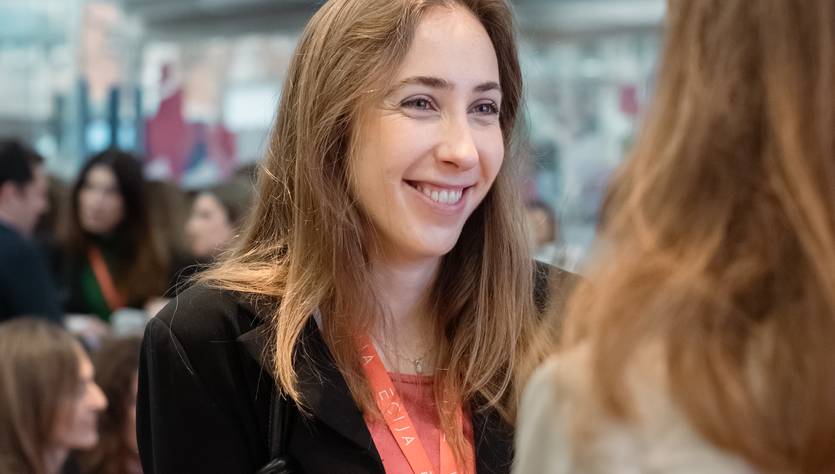 Una mujer sonriente en un evento social, conversando con otra persona.
