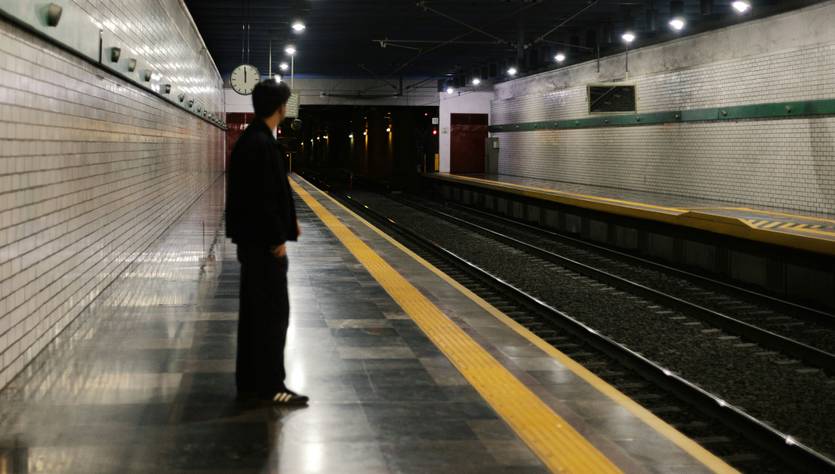 Un hombre espera en una estación de tren vacía y oscura.