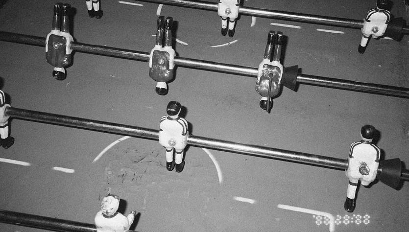 Una vista cenital de una mesa de futbolín con figuras de jugadores dispuestas en alineación.