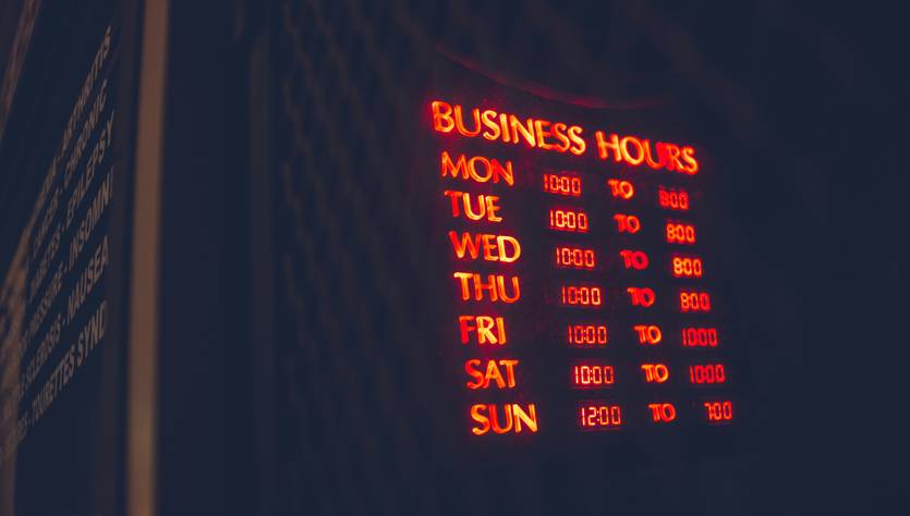 La imagen muestra un letrero de horarios de atención de un negocio con luces rojas.