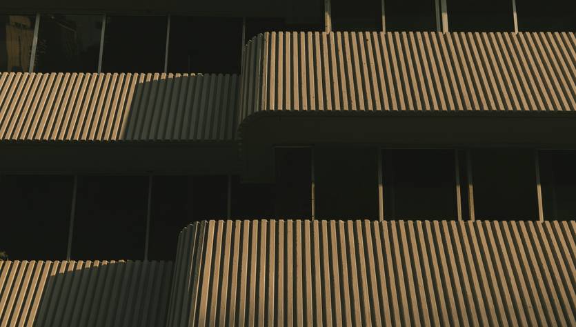 La imagen muestra un edificio moderno con balcones de líneas verticales y sombras marcadas por la luz del atardecer.