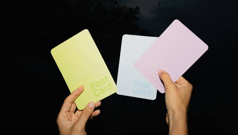 Tres tarjetas postales de colores sostenidas por manos en un entorno oscuro.