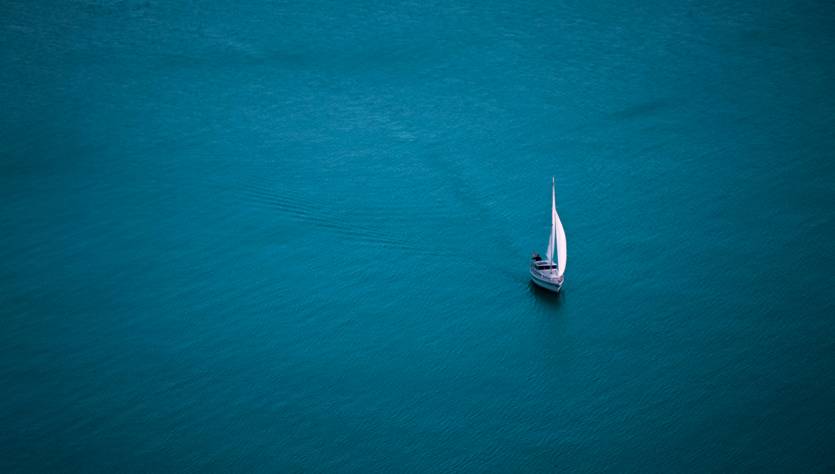 Un velero navega tranquilamente sobre aguas de color azul profundo.