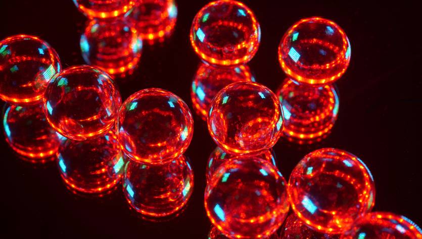 Esferas de vidrio rojas brillantes sobre una superficie reflejante.