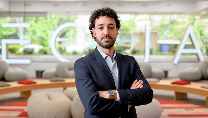 Un hombre con traje de negocios se encuentra de pie en un ambiente moderno y empresarial.