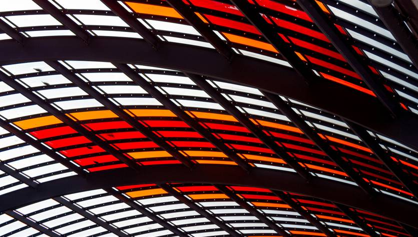 Una estructura arquitectónica con paneles de vidrio en tonos rojos, naranjas y amarillos.