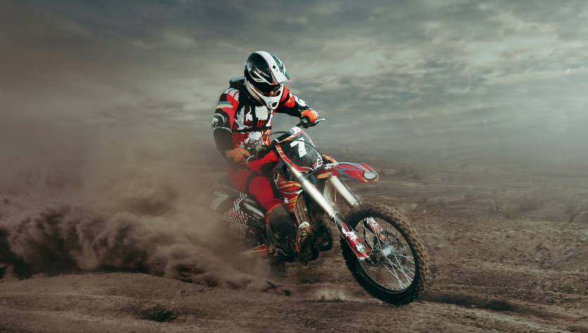 Un piloto de motocross realizando acrobacias en un terreno polvoriento.