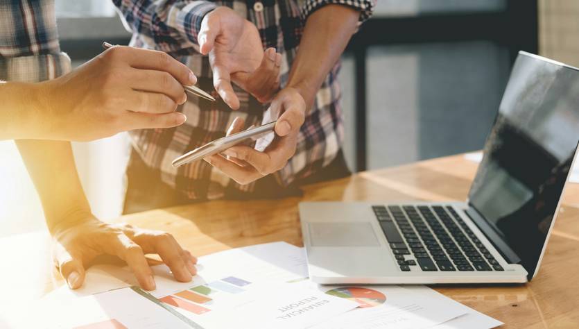 Dos personas discutiendo gráficos y datos sobre una mesa con una computadora portátil.