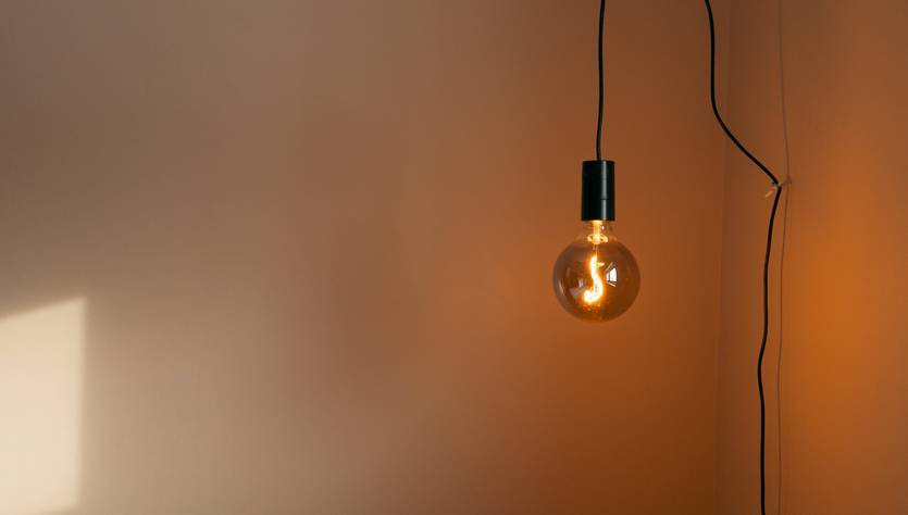 Una bombilla colgante emite luz suave en una pared clara.