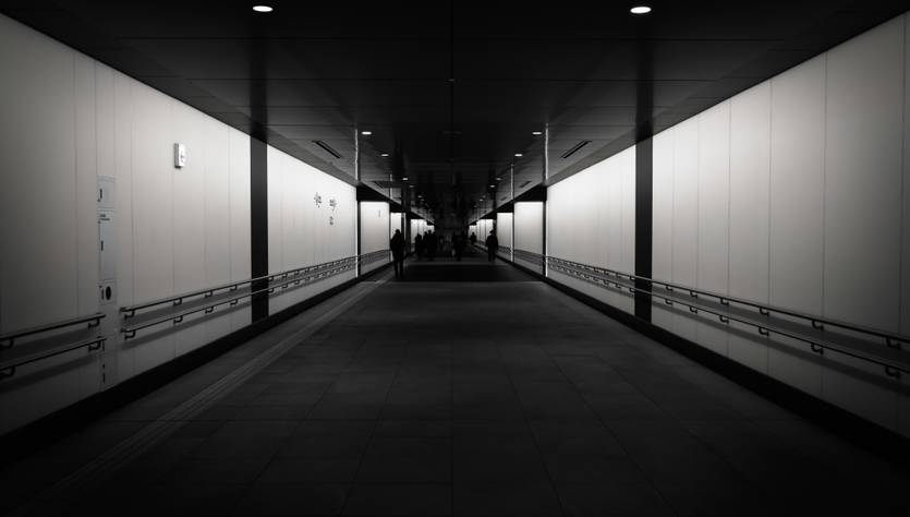 Pasillo oscuro con iluminación tenue y paredes blancas.