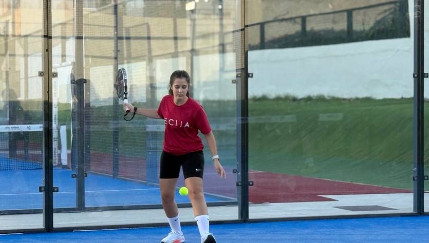 Una jugadora de pádel está en acción golpeando una pelota en una cancha cubierta.