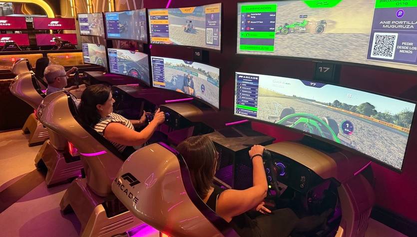 Tres personas están jugando a videojuegos de carreras en simuladores equipados con pantallas y volantes.