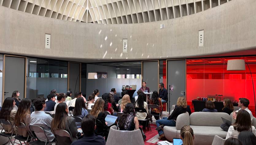 Una sala de reuniones con personas sentadas en sillas, mientras un orador se presenta frente al público.