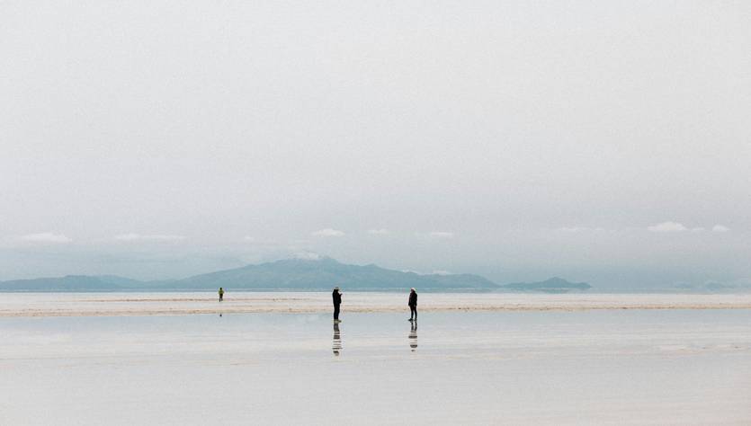 Dos personas caminan sobre una superficie reflectante en un paisaje nublado.