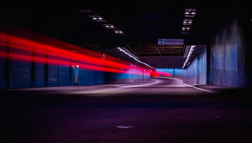 Una imagen de un túnel oscuro con luces rojas que se mueven rápidamente y paredes azuladas.