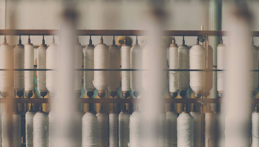 La imagen muestra una serie de bobinas de hilo ordenadas en una estantería.