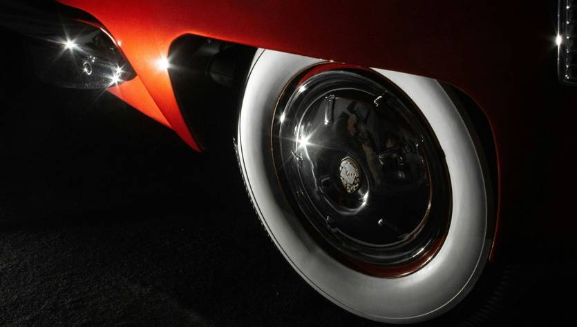 La imagen muestra una rueda de un automóvil clásico con detalles de brillo en la llanta y neumático blanco.
