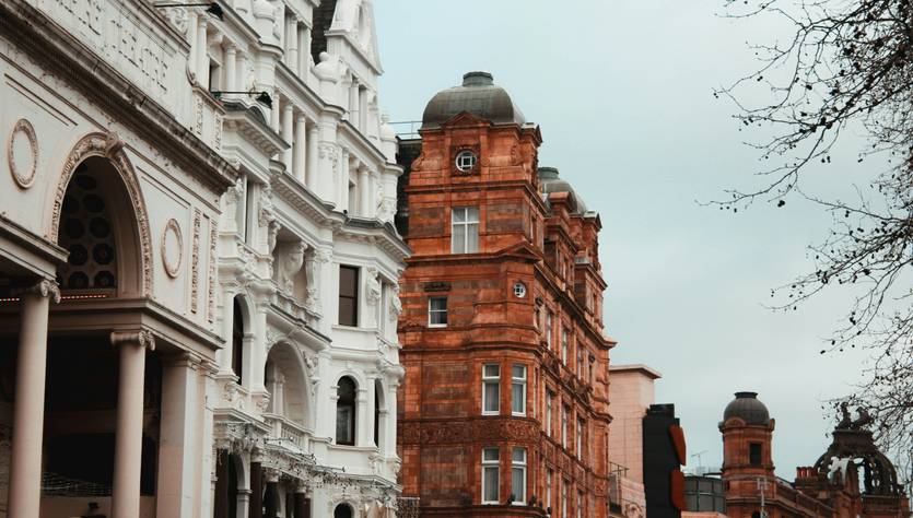 Una calle en una ciudad con edificios de arquitectura variada, incluyendo fachadas blancas y rojas.