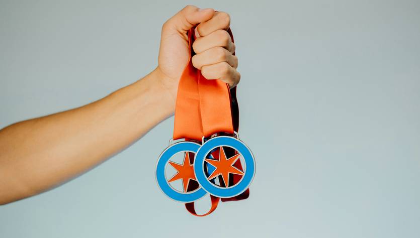 Un brazo sostiene dos medallas con cintas naranjas.