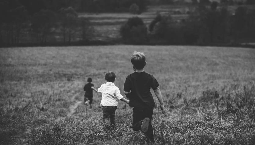 Un grupo de niños corre por un campo verde hacia un paisaje natural.