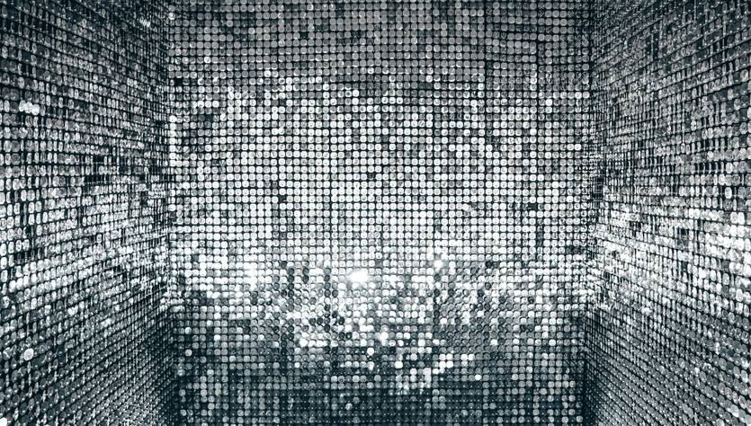 La imagen muestra un ambiente cubierto de superficies brillantes que reflejan luces en patrones deslumbrantes.