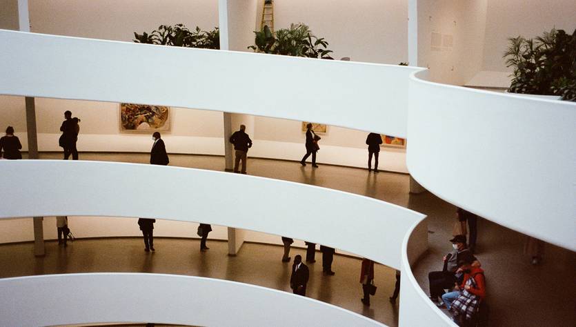 Vista interior de un museo con rampas y personas admirando las obras en las paredes.