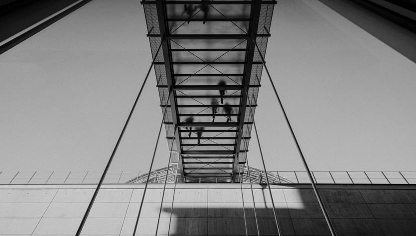 Una pasarela de vidrio suspendida sobre una estructura moderna con sombras proyectadas.