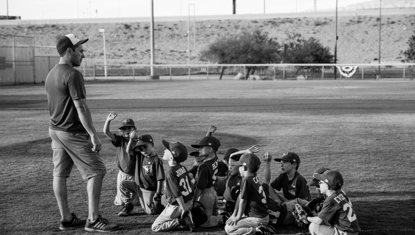 Un entrenador charla con su equipo de jóvenes jugadores de béisbol en un campo.