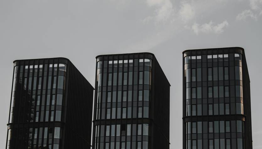 Tres edificios modernos con fachadas de vidrio y un cielo nublado de fondo.