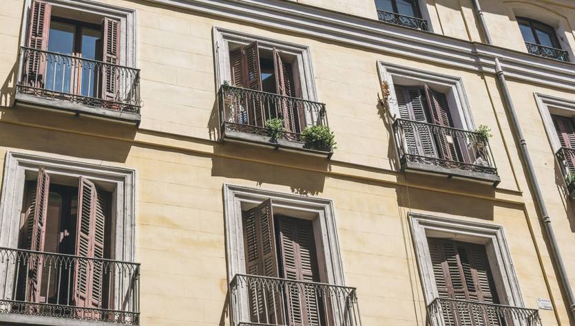 La imagen muestra la fachada de un edificio con varios balcones y ventanas con persianas de madera.