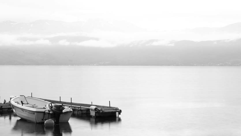 Una tranquila escena en blanco y negro de un bote amarrado en un muelle junto a aguas serenas.