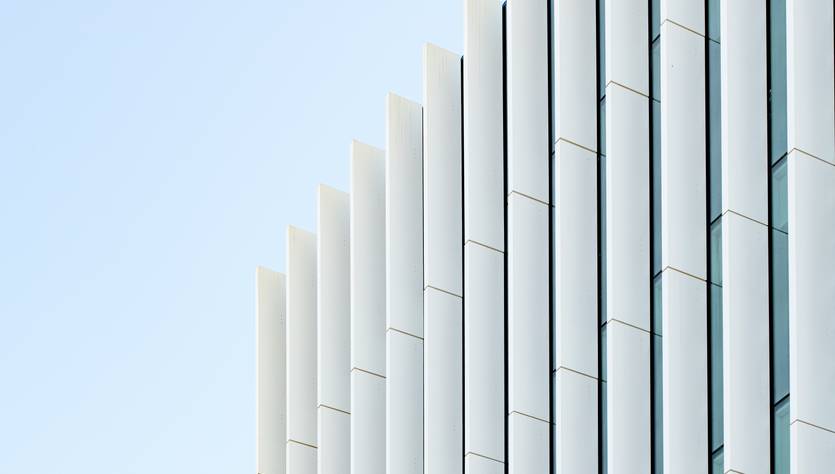 La imagen muestra un edificio modernista con una fachada de paneles blancos y líneas limpias.