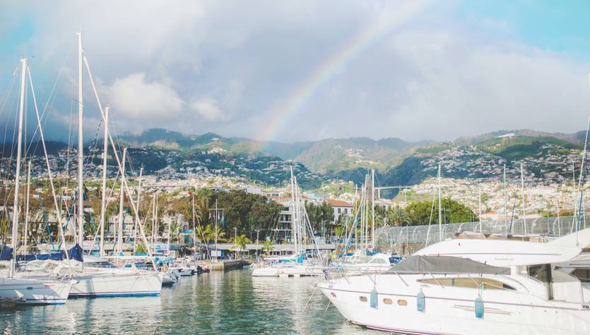 Una vista del puerto con yates y un arcoíris al fondo.