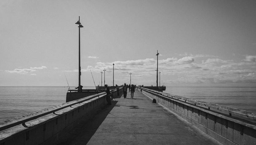 Un muelle se extiende hacia el mar con varias personas caminando por él bajo un cielo nublado.
