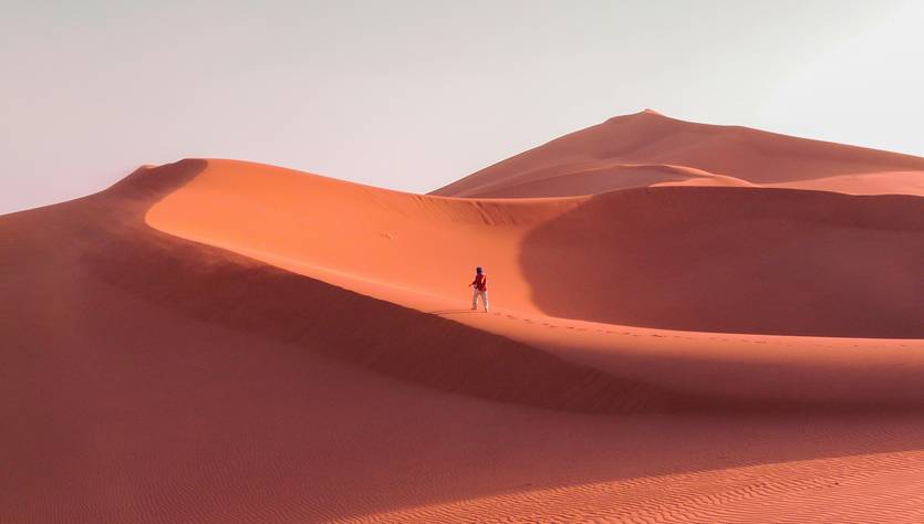 Una persona camina sola sobre las dunas de arena de un desierto al atardecer.