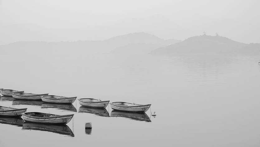 Una serie de botes de remos se reflejan en un lago tranquilo y brumoso.