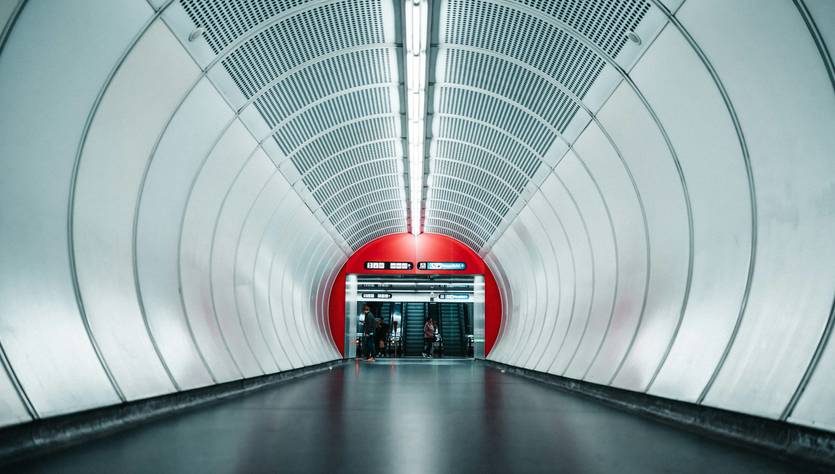 Un túnel moderno de estación de metro con iluminación blanca y paredes curvas de color plateado.