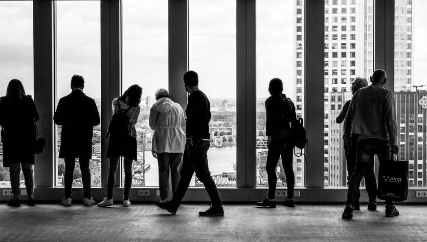 Un grupo de personas observa la ciudad a través de grandes ventanales en un edificio alto.