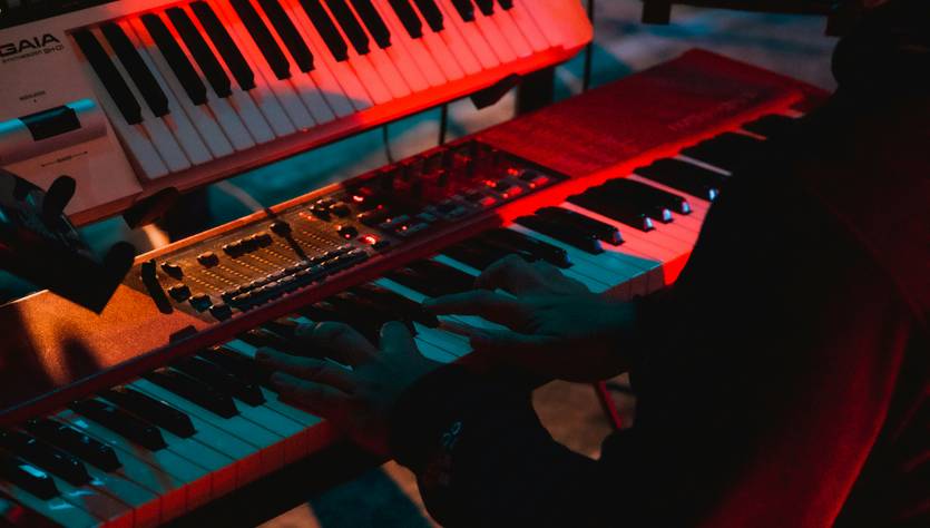 Una persona toca varios teclados en un ambiente iluminado con luces rojas y azules.