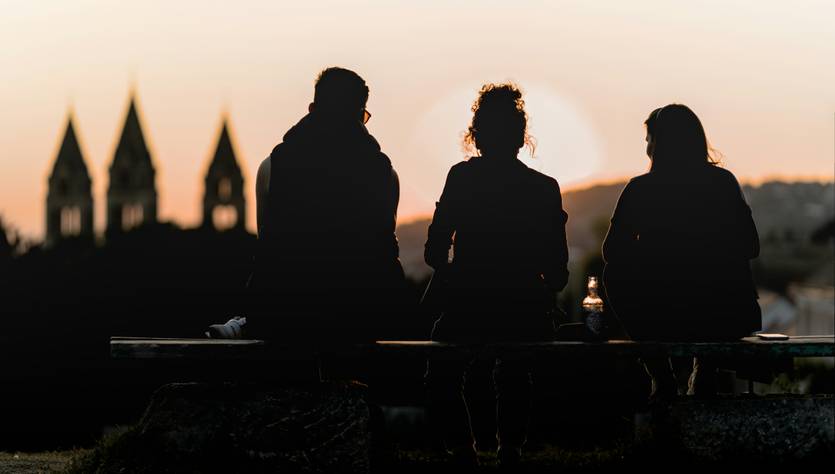 Tres personas sentadas en un banco observando el atardecer.