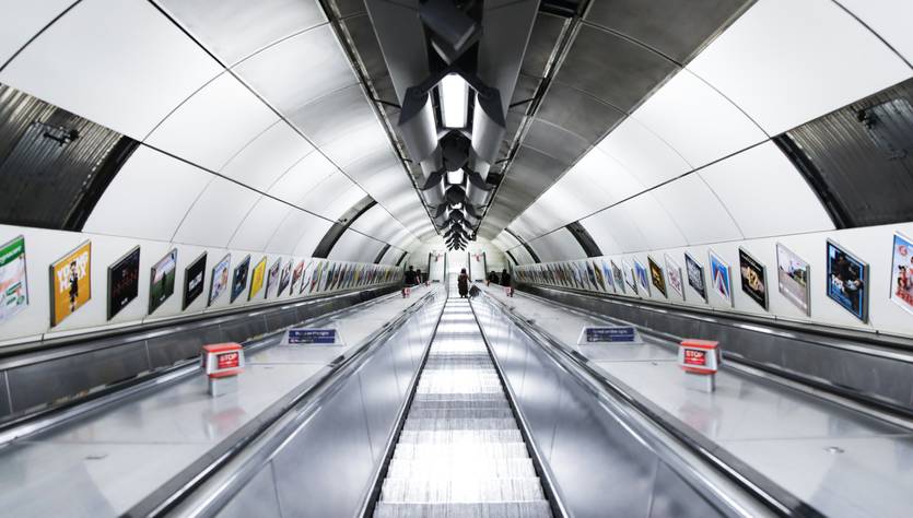Un pasillo en una estación de metro con escaleras mecánicas y obras de arte en las paredes.