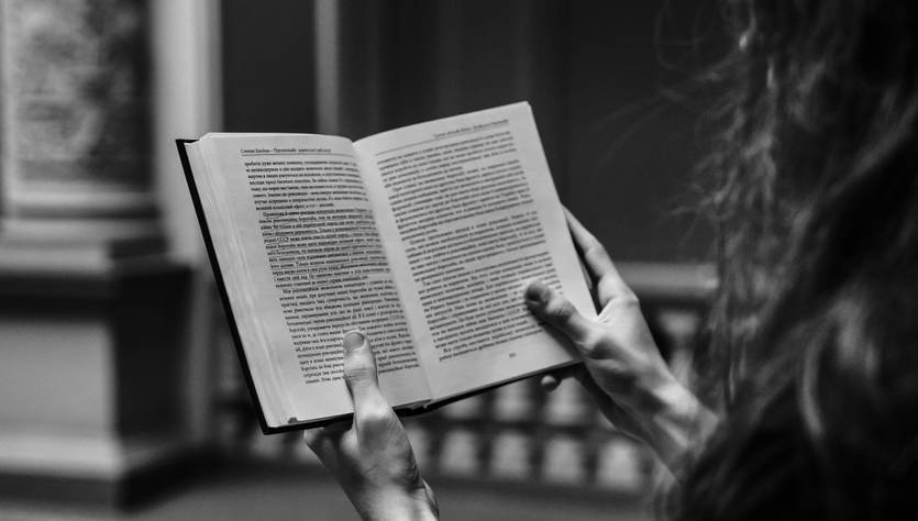 Una persona sostiene un libro abierto mientras lee en un ambiente sombrío.