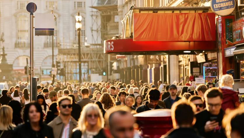 Una multitud de personas camina por una calle iluminada por el sol en un ambiente urbano.